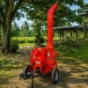 Red portable wood chipper on wheels in a grassy yard with trees and sheds in the background.