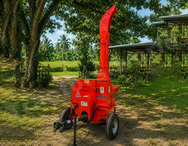 Red portable wood chipper on wheels in a grassy yard with trees and sheds in the background.