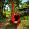 Red Massive wood chipper in a rural yard, with a raised chute and a path, trees, and a shed in the background.