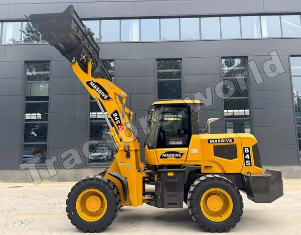 Yellow telescopic loader with raised bucket and large tires, labeled MASSIVE 845, parked in front of a dark modern building.