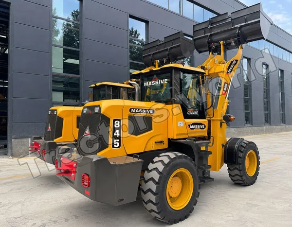 Yellow heavy construction loader with a raised front bucket and large off-road tires, parked outside a dark-gray industrial building; labeled MASSIVE with model 845 on the side.