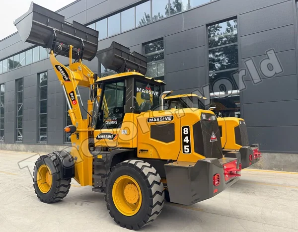 Yellow heavy front-end loader with oversized bucket raised, parked in front of a modern dark-gray building; labeled MASSIVE and 845 on the side, large rugged tires visible.