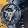 Steering wheel and dashboard of a yellow construction vehicle; gauge cluster, switches, and foot pedals visible.