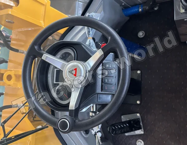 Steering wheel and dashboard of a yellow construction vehicle; gauge cluster, switches, and foot pedals visible.